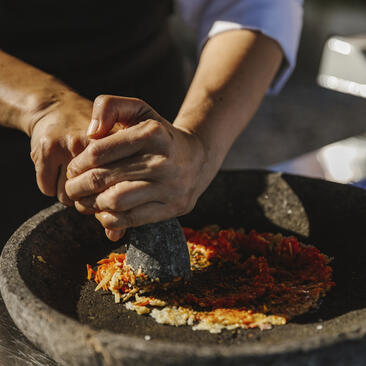 Hands crushing spices in a stone mortar during a cooking class at Amankila resort, Bali.