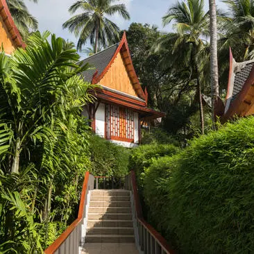 Stone steps leading to a teak pavilion at Amanpuri, surrounded by lush tropical gardens and palm trees.