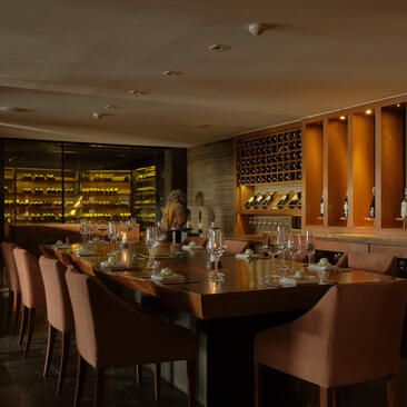 Salone privato per cene con tavolo scuro, sedie in pelle e illuminazione calda ad Amanpuri, resort in Thailandia.