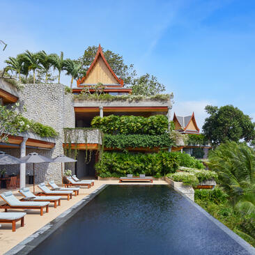 Amanpuri villa with golden-roofed pavilion overlooking a reflecting pool, surrounded by lush gardens.