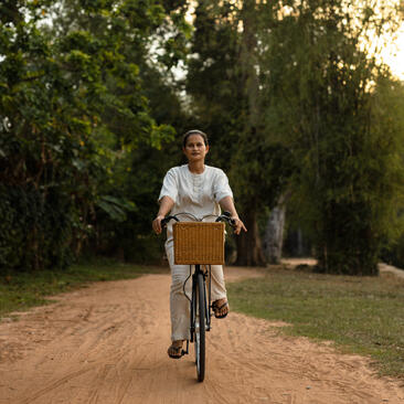A guest rides a bicycle along a tree-lined dirt path at Amansara.
