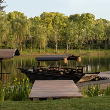 Traditional wooden boat on West Lake at Amanyangyun, surrounded by weeping willows and calm waters.