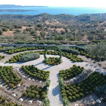 Vue aérienne d'Amanzoe, un resort en Grèce, avec jardins en terrasses et rivière sinueuse.