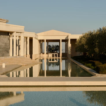 Amanzoe pavilion reflected in still pool water at sunset, with cypress trees framing the Peloponnese landscape.