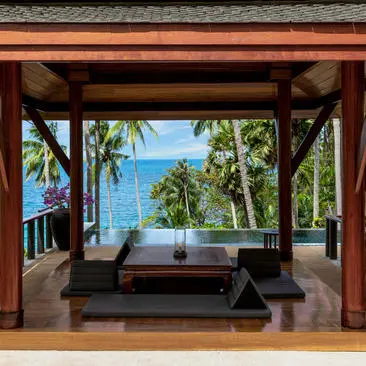 Pavilion overlooking the ocean at Amanpuri, with wooden beams framing a view of turquoise waters and palm trees.