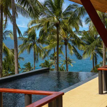 Infinity pool overlooking the ocean at Amanpuri, framed by palm trees and a wooden pavilion.