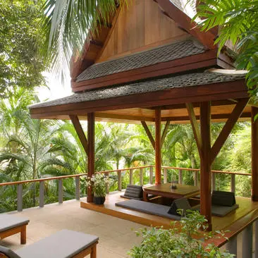 Wooden sala pavilion with pitched roof nestled among tropical greenery at Amanpuri, featuring a restful seating area beneath the structure.