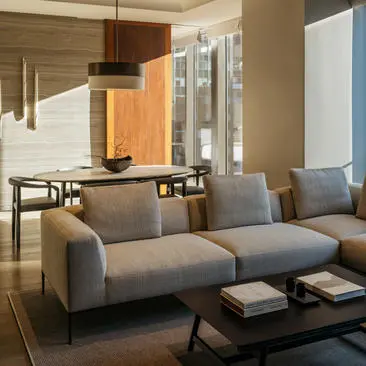 Grey modular sofa in bright living room at Aman New York with wooden cabinetry and floor-to-ceiling windows.