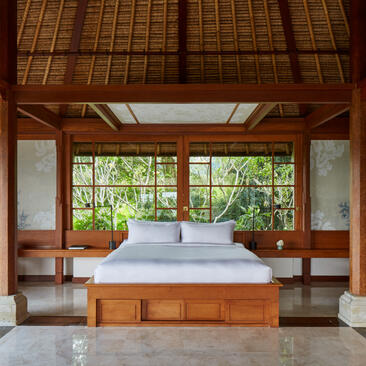 Principal bedroom at Amandari with wooden platform bed and garden views through large doors.