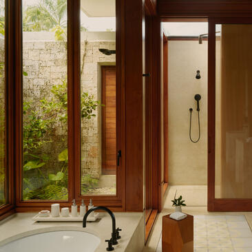 Bathroom at Amanera with walk-in shower, freestanding tub, and garden views through wooden-framed doors.
