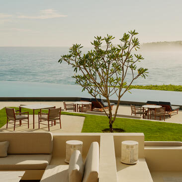 Amanera's beachfront bar terrace with dining tables, a solitary tree, and Caribbean Sea views.