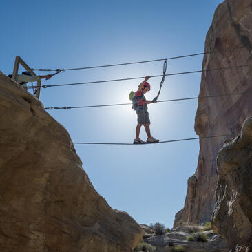 Child navigating via ferrata cable course between rock faces at Amangiri, Utah.