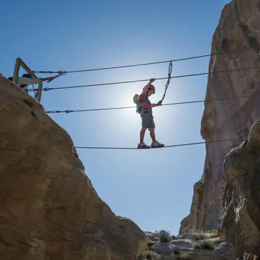 Bambino attraversa una via ferrata sospesa tra due pareti rocciose ad Amangiri.
