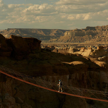 Climber traversing a via ferrata route across red rock formations at Amangiri, Utah.