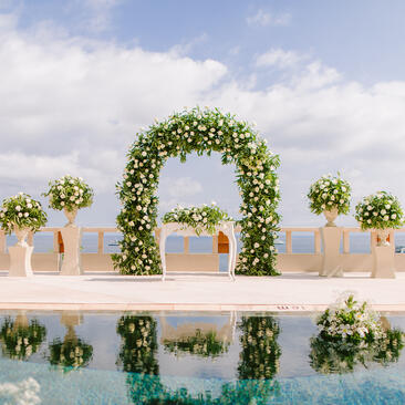 Floral archway and ivy-draped pedestals arranged beside a reflecting pool at Amankila, ready for a celebration.