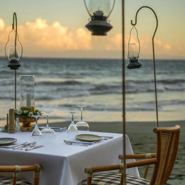 Dining table set for two at Amankila with ocean view at sunset, lanterns overhead.