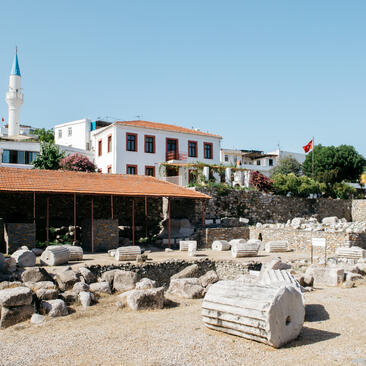 Ancient Bodrum ruins with scattered marble columns and architectural fragments in front of Amanruya's whitewashed buildings.