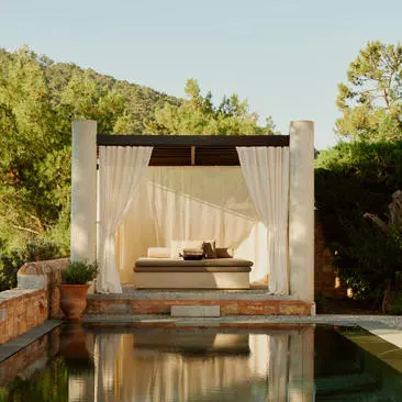 Pavilion with cream curtains overlooking a reflecting pool in Amanruya's garden at dusk.