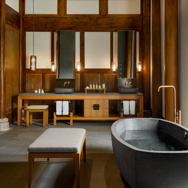 Antique villa bathroom at Amanyangyun with dark stone soaking tub, wooden cabinetry and mirror panels.