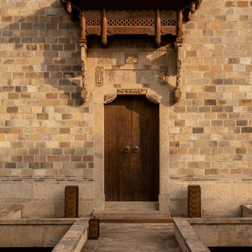 Antique villa entrance door at Amanyangyun, with dark wooden door set in terracotta brick wall and stone bollards.