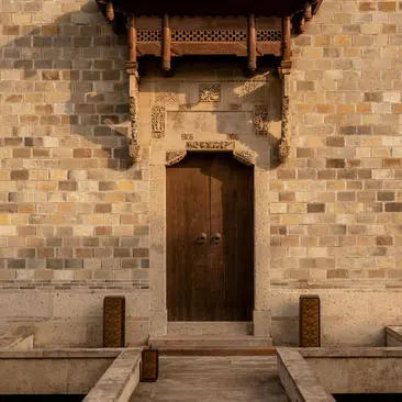 Antique villa entrance door at Amanyangyun, with dark wooden door set in terracotta brick wall and stone bollards.