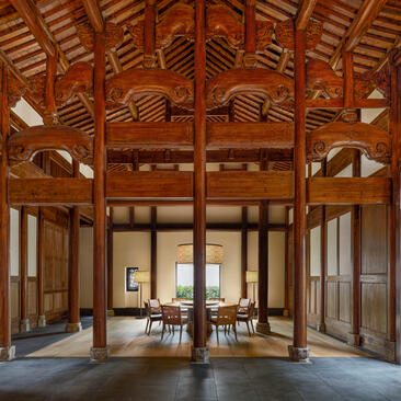 Amanyangyun villa dining area with timber ceiling, wooden screens and central table beneath soaring rafters.