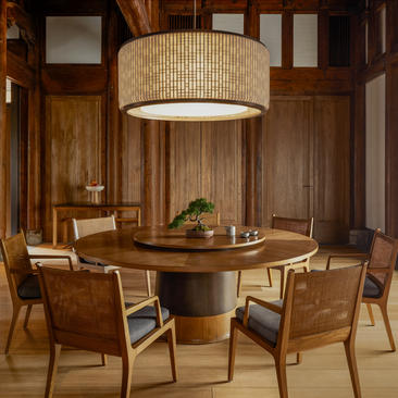 Amanyangyun villa dining area with round wooden table, upholstered chairs, and cylindrical pendant light.
