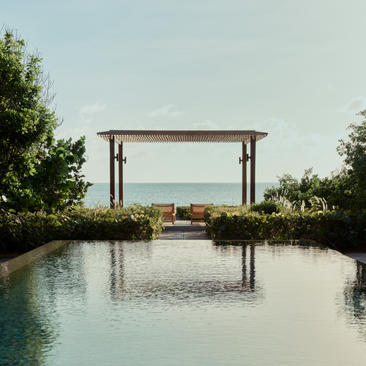 Amanyara pavilion with wooden pergola overlooking a tranquil lagoon and turquoise sea beyond.