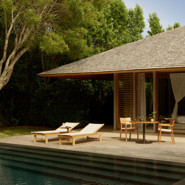 Deluxe pool pavilion at Amanyara with wooden loungers and dining chairs on a stone terrace overlooking a plunge pool, surrounded by tropical greenery.
