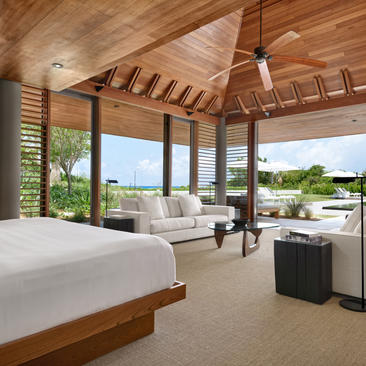 Five-bedroom beach sala villa at Amanyara with wooden ceiling, bed, and ocean views through floor-to-ceiling windows.