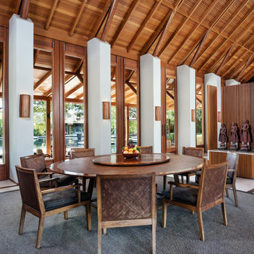 Dining area at Amanyara with wooden ceiling, central stone table, and woven chairs beneath white columns.