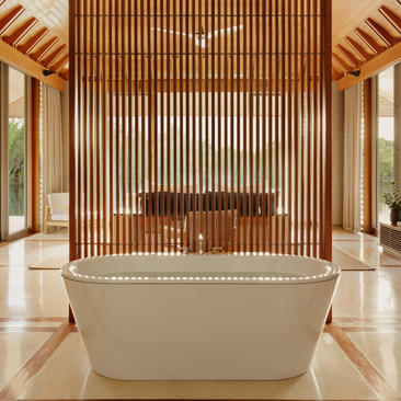 Four-bedroom villa bathroom at Amanyara with freestanding stone bathtub and wooden slat feature wall.