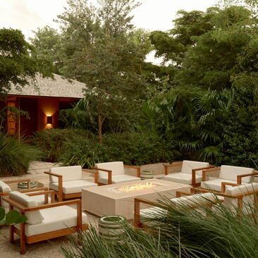 アマンヤラ・リゾートの四寝室トランクイリティヴィラの屋外シーティングエリア。木製フレームの椅子とクッションが緑に囲まれている。