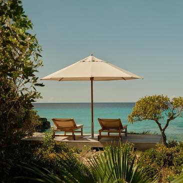 Ocean Cove Pavilion at Amanyara with lounge chairs beneath a cream parasol overlooking turquoise waters.