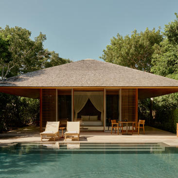 Pool pavilion at Amanyara overlooking turquoise waters, with thatched roof and wooden furnishings.
