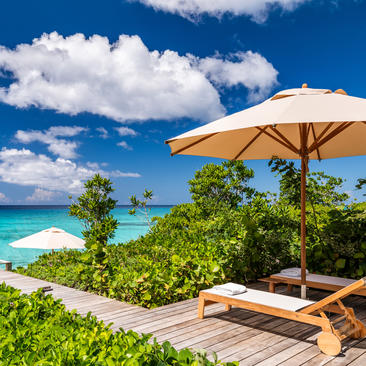 Six-bedroom beach sala villa at Amanyara with wooden deck, loungers, parasol and turquoise waters beyond.