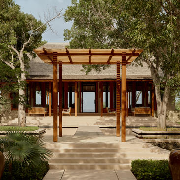 The Artists Villa at Amanyara features a wooden pergola structure sheltering the entrance, with tropical vegetation and manicured gardens.