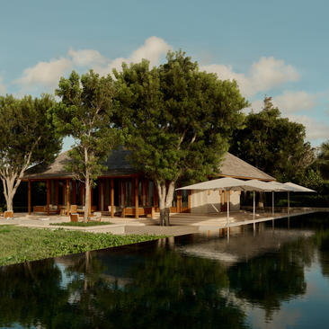 The Artist's Villa at Amanyara with wooden pavilions reflected in still water, surrounded by lush trees.