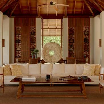Symmetrical studio interior at Amanyara with wooden ceiling, cream sofas, and central fan artwork.