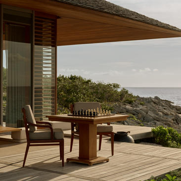 Wooden deck at Amanyara with seating area overlooking hillside and ocean view.