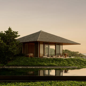 The Artists Villa at Amanyara with pyramid-shaped roof reflected in still water at dusk.