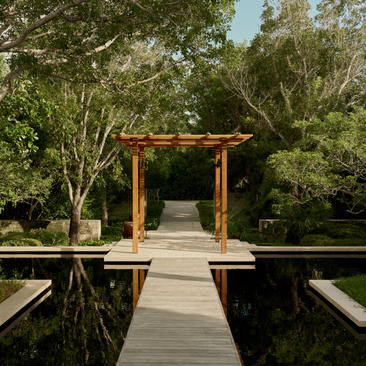Wooden walkway leading to a pavilion at Amanyara, surrounded by tropical vegetation and water features.