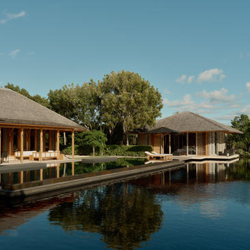 Three-bedroom villa with thatched pavilions reflected in still lagoon water at Amanyara, Turks and Caicos.