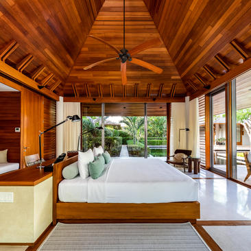 Bedroom 6 at Amanyara villa with wooden ceiling, white bedding, and garden views through glass doors.