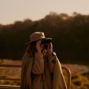Safari guide at Aman-i-Khas observing wildlife through binoculars at dusk.