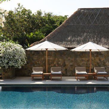 Resort swimming pool at Aman Villas at Nusa Dua, Indonesia, with thatched pavilion and loungers.