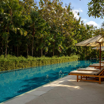 Resort swimming pool at Aman Villas at Nusa Dua, flanked by loungers and tropical trees.