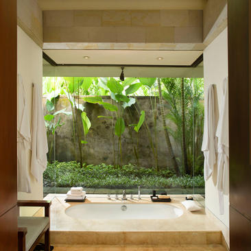 Bedroom at Aman Villas at Nusa Dua with garden view through open doors and tropical plants.