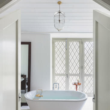 Bathroom at Amangalla with freestanding bathtub beneath latticed window and pendant light.
