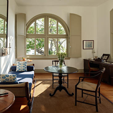 Sunlit principal bedroom at Amangalla with arched window, blue upholstered chair, and period furnishings.
